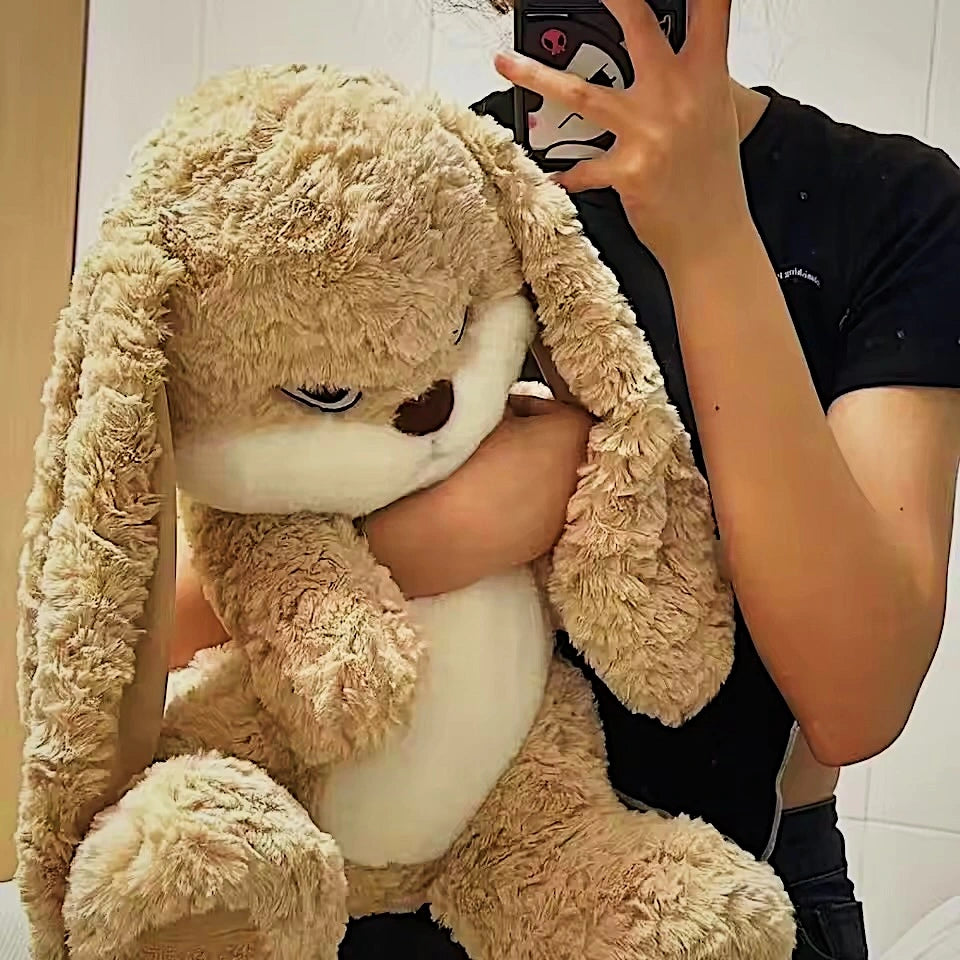 Person holding a large beige plush bunny toy in front of a mirror.