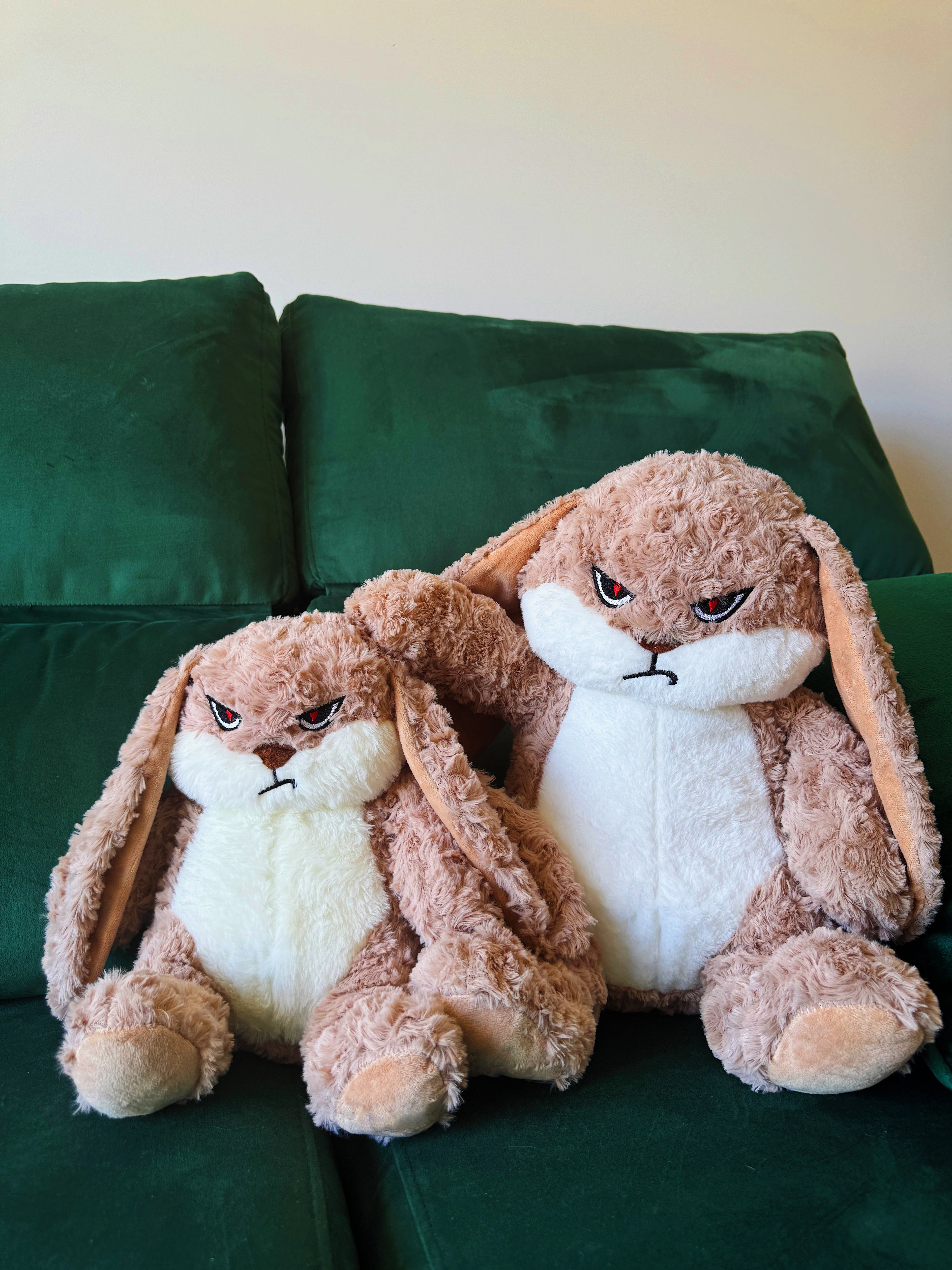 Two plush bunny toys with angry expressions on a green couch.